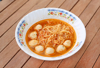 Instant noodles with meat balls in ceramic bowl against wooden plank.