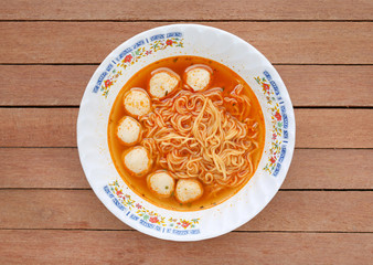 Top view instant noodles with meat balls in ceramic bowl against wooden plank.