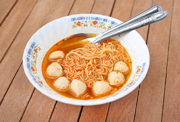 Instant noodles with meat balls in ceramic bowl against wooden plank.