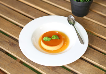 Caramel custard cake with peppermint leaf in white plate on wooden table.