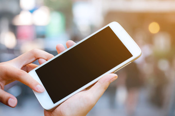 woman hand hold and touch screen smart phone,tablet,cellphone on shopping street background with sunset lighting. 