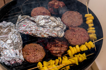 Grilled meat on a charcoal griddle accompanied by onions in foil and pineapple.