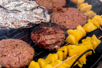 Grilled meat on a charcoal griddle accompanied by onions in foil and pineapple.