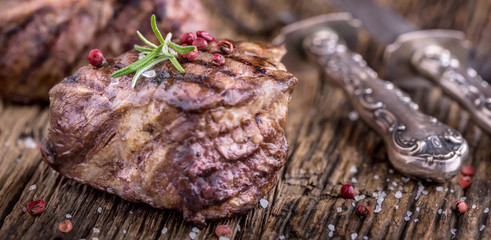 Grilled beef steak with rosemary, salt and pepper on old cutting board. Beef tenderloin steak.