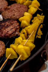 Grilled meat on a charcoal griddle accompanied by onions in foil and pineapple.