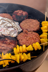 Grilled meat on a charcoal griddle accompanied by onions in foil and pineapple.