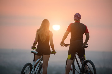 Rear view of man and woman on the mountain bikes enjoying the sunset. Bright sun in between. Blurred background. Close-up