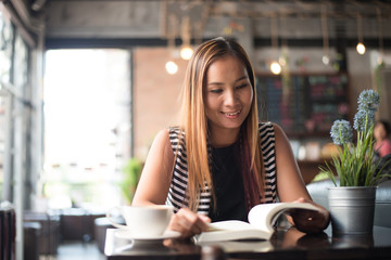 Asian woman relaxing and reading a book in the cafe. Women lifestyle concept.