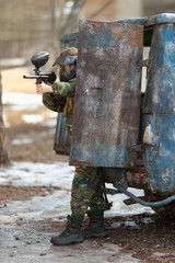 girl playing paintball in overalls with a gun.