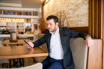 Businessman is sitting in restaurant and checking his phone