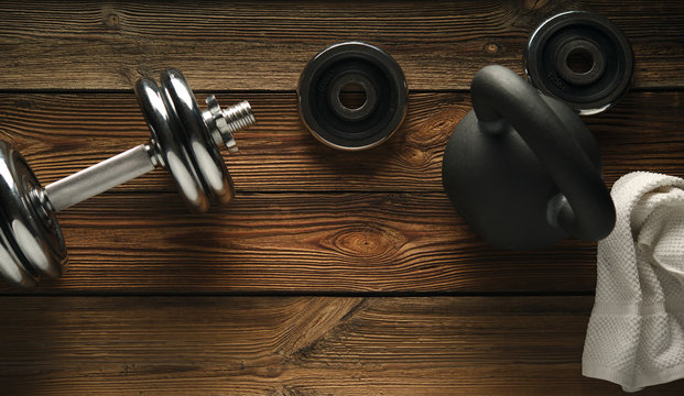 Top view of black iron kettlebell, dumbbell and white towel on wooden floor Sport background with copyspace