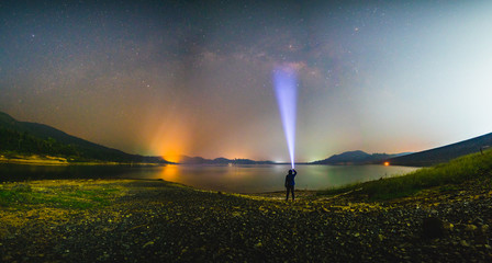 Silhouette man with flashlight and Milky way galaxy at lake