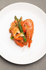 rice with shrimp and asparagus in a tomato sauce on a white plate on a gray background.