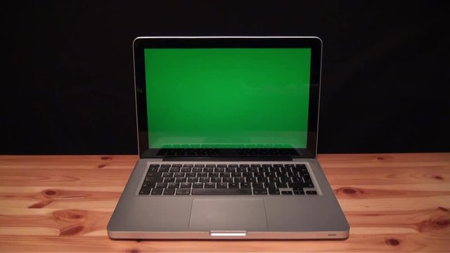 Laptop with green screen chroma on a wooden table and black background. Adrian
