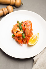 rice with shrimp and asparagus on a white plate with lemon, pepper, salt shaker on a gray background.