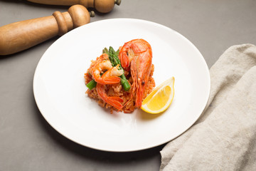 rice with shrimp and asparagus on a white plate, pepper, salt shaker on a gray background.