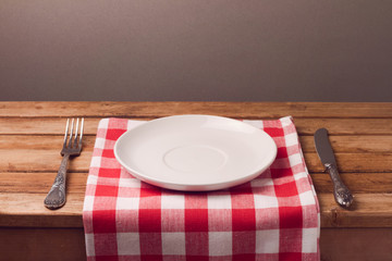 Empty plate with tablecloth and silverware on wooden table