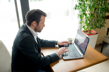 Man is sitting in cafe, enjoying cup of coffee and surfing net