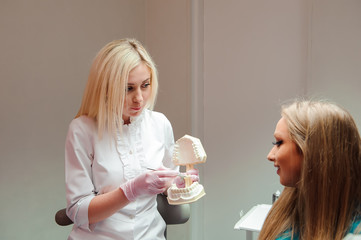 Obraz na płótnie Canvas female dentist talking to patient, showing dental jaw model in dental clinic office.