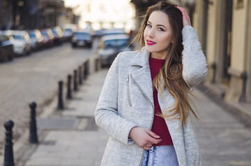 Outdoor portrait of a young beautiful happy smiling woman posing on the street wearing cashmere sweater and coat, looking at the camera. 