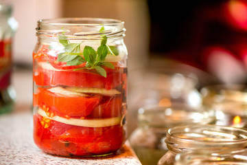 Fototapeta na wymiar Canning fresh tomatoes with onions for winter in jelly marinade. A shot of basil leaves on top of a red ripe tomato slices and onions being put in jar.