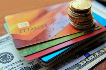 Stack of credit cards with american dollars and coins on a wooden background, close-up view.