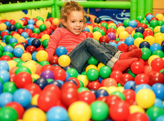 Fototapeta na wymiar Cheerful child playing inside ball pit swimming pool - Little girl having fun in baby playground indoor - Childhood concept - Focus on female face - Warm filter