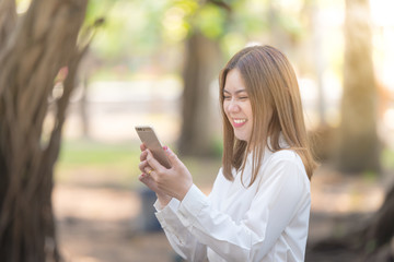 Fototapeta premium Young Happy business woman Laugh and smiling with smart phone. Beautiful asian girl with mobile phone. On Forest sunlight background