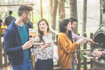 Group of happy friends cooking and eating at barbecue dinner outdoor