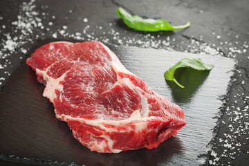 raw beef steak with rosemary and peppers on dark stone