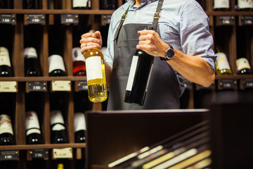 Young sommelier holding bottle of red wine in cellar