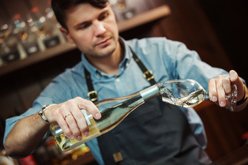 Male sommelier pouring white wine into long-stemmed wineglasses.