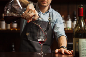 Sommelier pouring wine into glass from mixing bowl. Male waiter