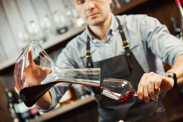 Sommelier pouring wine into glass from mixing bowl. Male waiter