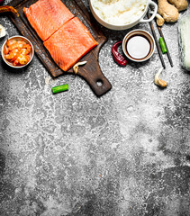 Asian food. Boiled rice with a piece of salmon and a variety of ingredients. On rustic background .