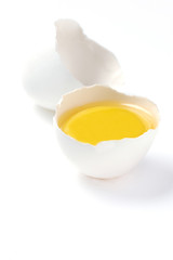 Broken raw egg showing the egg yolk over white background 