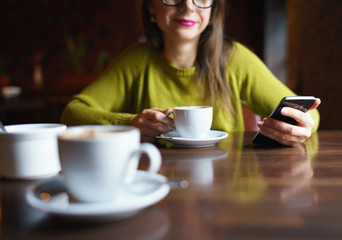 Young woman drinking coffee and using smartphone in cafe