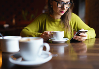 Young woman drinking coffee and using smartphone in cafe