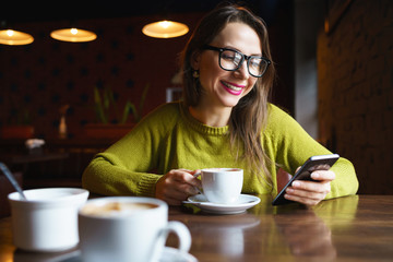 Young woman drinking coffee and using smartphone in cafe