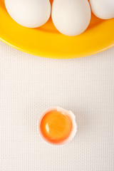 yellow  plate with raw uncooked  white eggs and a half of egg with egg yolk in front