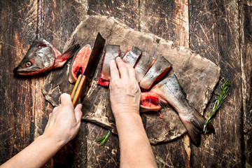 Obraz premium Raw fish. Cutting fresh salmon women's hands. On the old wooden table.
