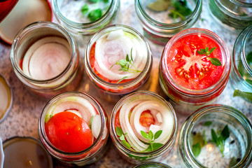 Canning fresh tomatoes with onions for winter in jelly marinade. A shot of basil leaves on top of a red ripe tomato slices and onion rings being put in jar.

