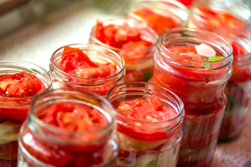 Canning fresh tomatoes with onions for winter in jelly marinade. A shot of basil leaves on top of a red ripe tomato slices and onions being put in jar.

