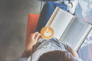 A girl reading book with drinking coffee latte with heart pattern on sofa in cafe
