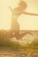 Carefree woman jumping in the sunset light on the beach. Vacation happy living concept retro color shot copyspace