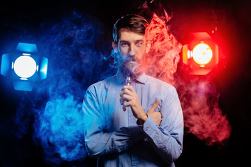 Young guy with a beard vaping and releases a cloud of vapor. hipster vaper smoke vaporizer.