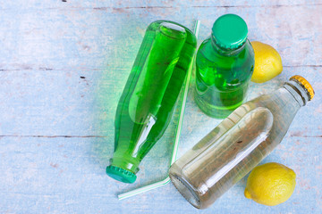  Soft drinks. Fruit lemonade in glass bottles and two lemons on a light wooden table.