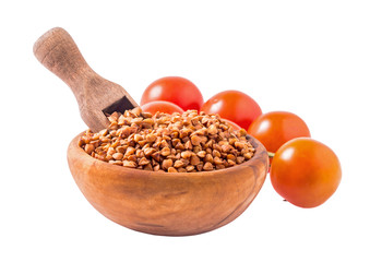 Wooden bowl of uncooked buckwheat groats with scoop and tomatoes