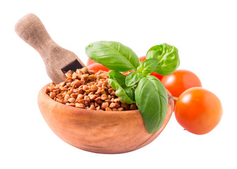 Wooden bowl of uncooked buckwheat groats with scoop and basil leaves. Isolated on white background