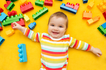 Little baby playing with lots of colorful plastic blocks constructor on a yellow background.